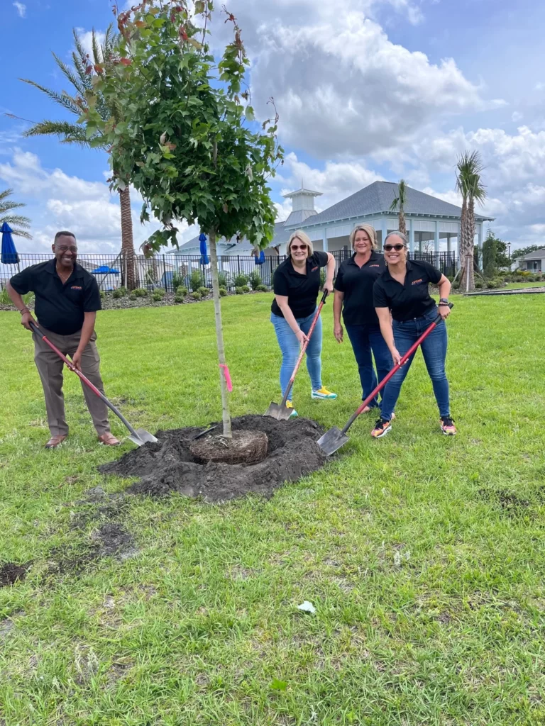 Three women and one man joyfully planting a tree in the garden in front of a home at Avalon Park, Tavares Homes.
