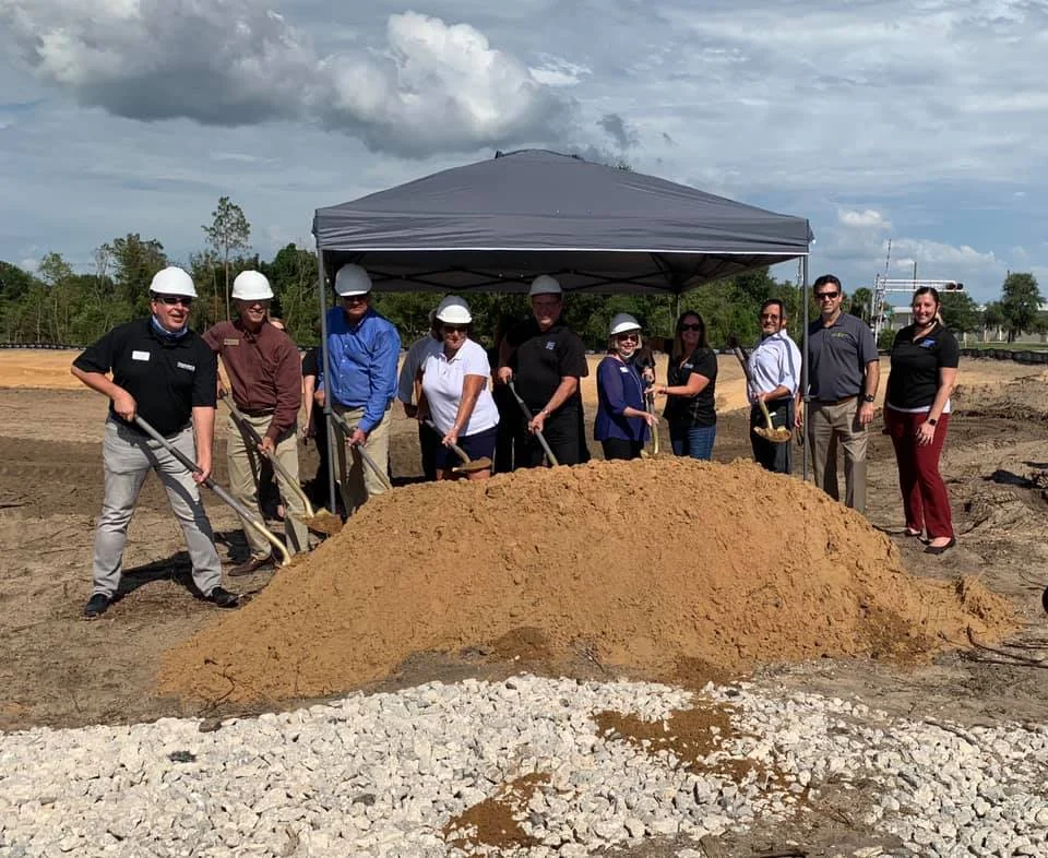 People engaged in a communal digging activity on the lush green grounds of Avalon Park Tavares, fostering community and connection amidst the scenic natural beauty.