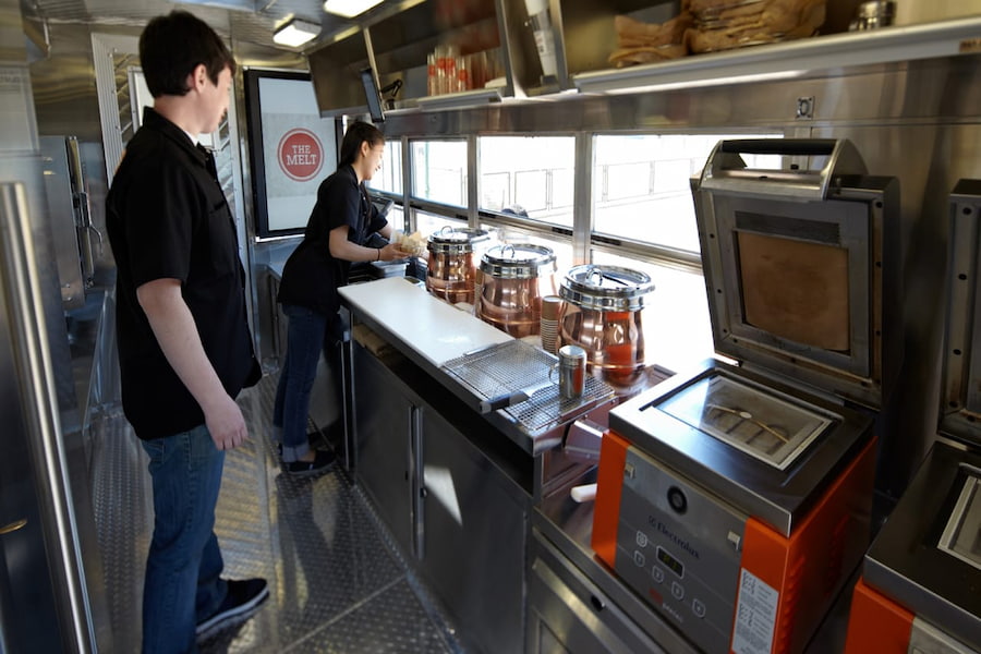 A couple cooking in a compact food truck kitchen, using a stove and oven to prepare delicious meals.